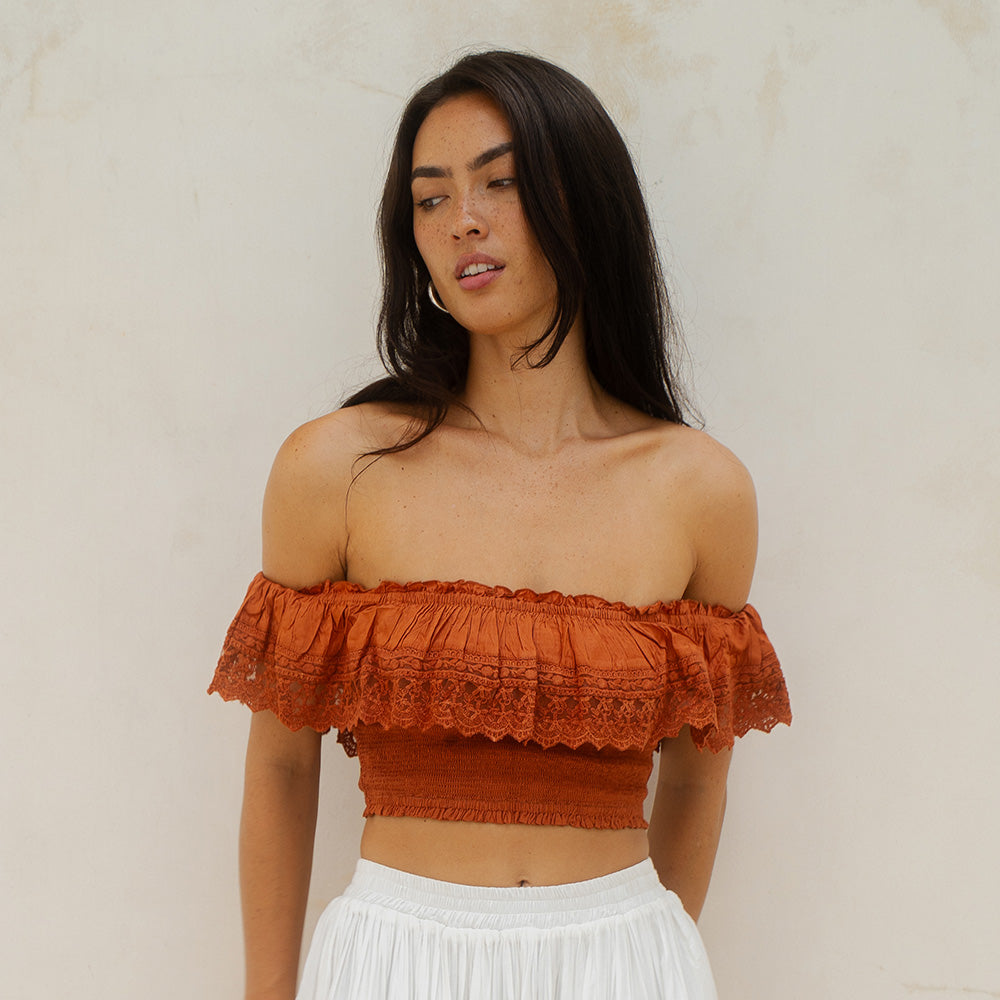 Woman wearing an off-shoulder rust-colored top against a beige background