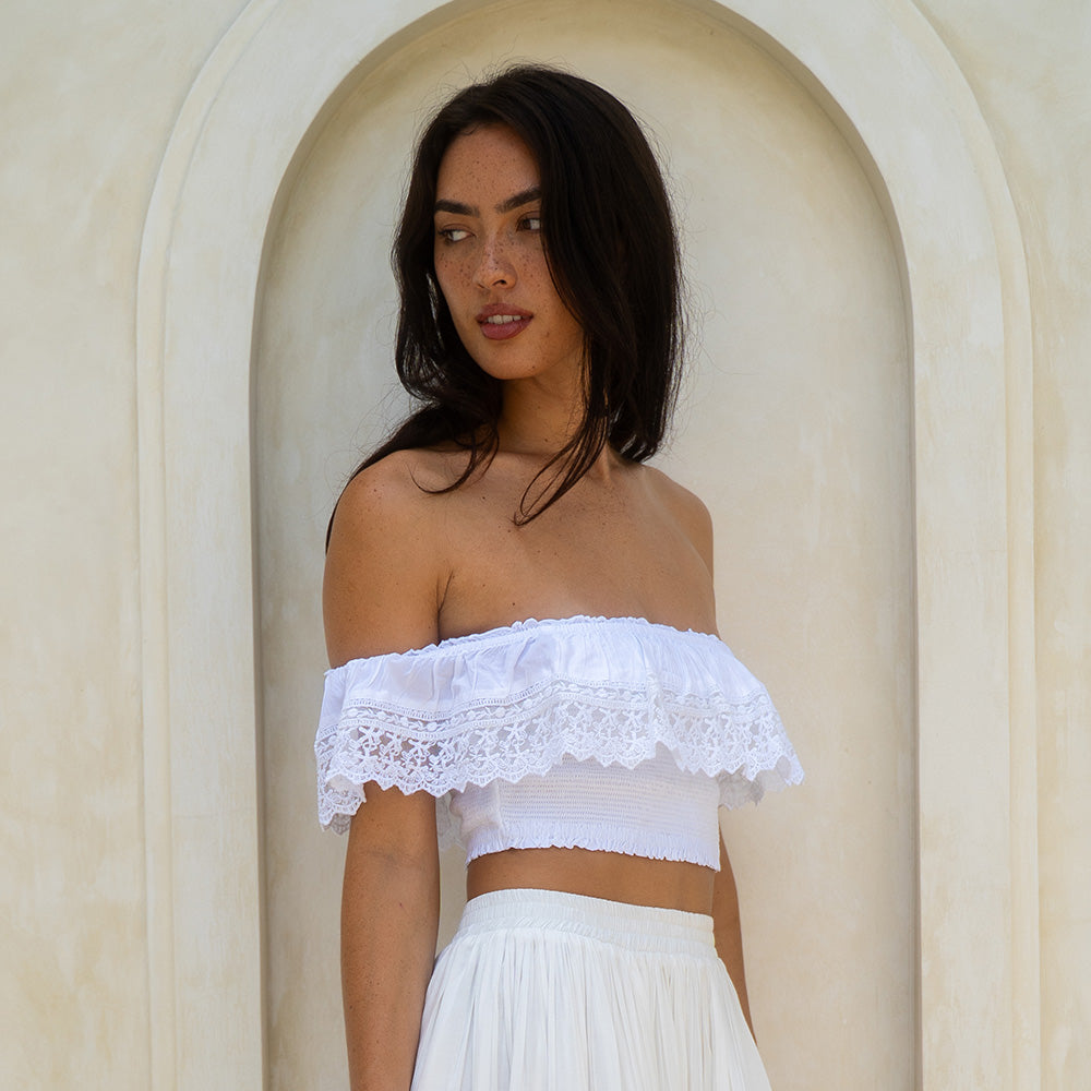 Woman wearing a white off-shoulder top and skirt against a beige wall.