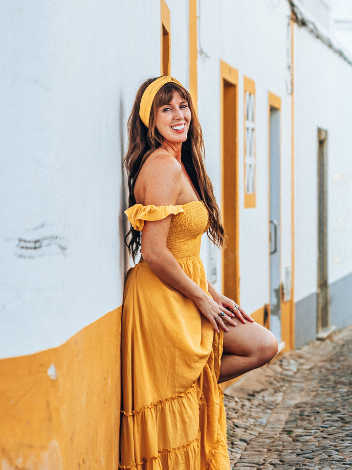 Woman in a yellow dress and headband standing against a white wall with yellow accents.