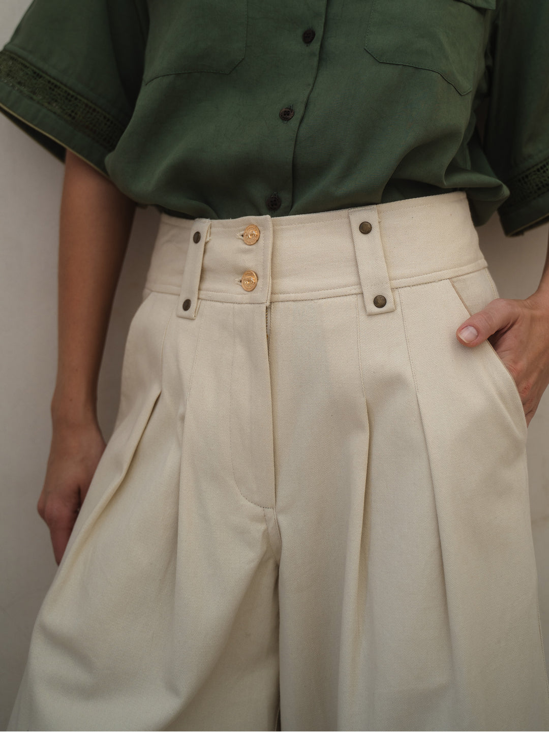 Person wearing a green shirt and beige high-waisted pants with gold buttons.