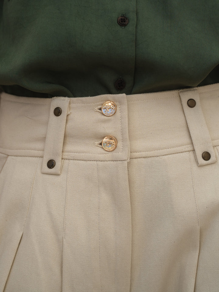 Close-up of beige pants with gold buttons and a green shirt in the background