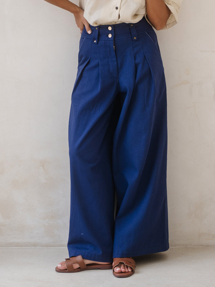 Person wearing blue wide-leg pants and a beige shirt against a neutral background