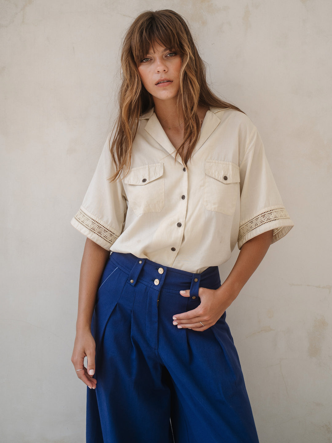 Woman wearing a beige shirt and blue pants against a plain background