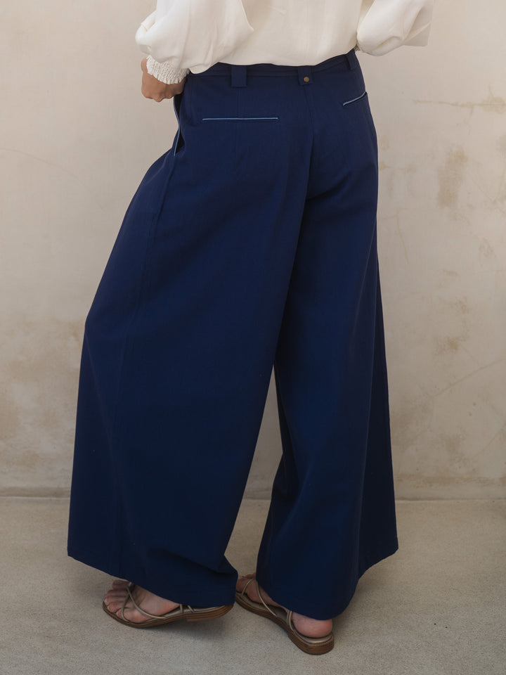 Person wearing navy wide-leg pants and a white shirt against a beige background