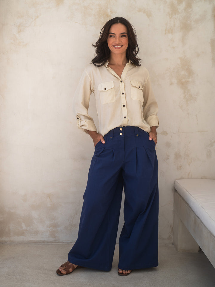 Woman wearing a beige shirt and blue pants against a textured wall.