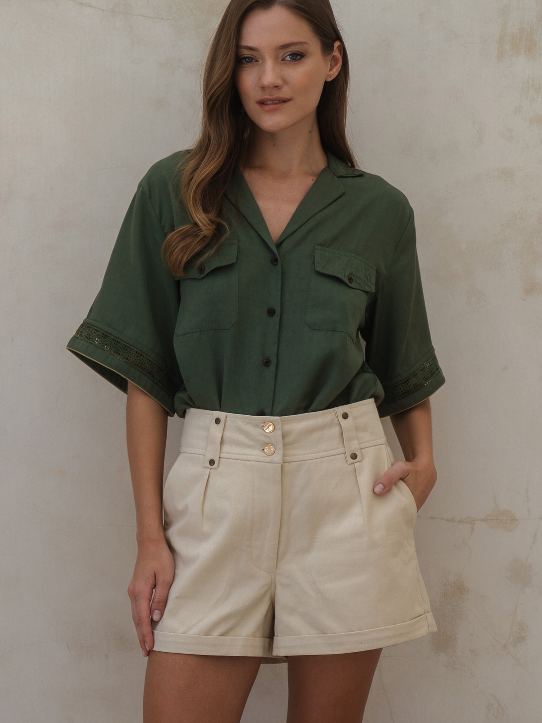 Woman wearing a green shirt and beige shorts against a plain background