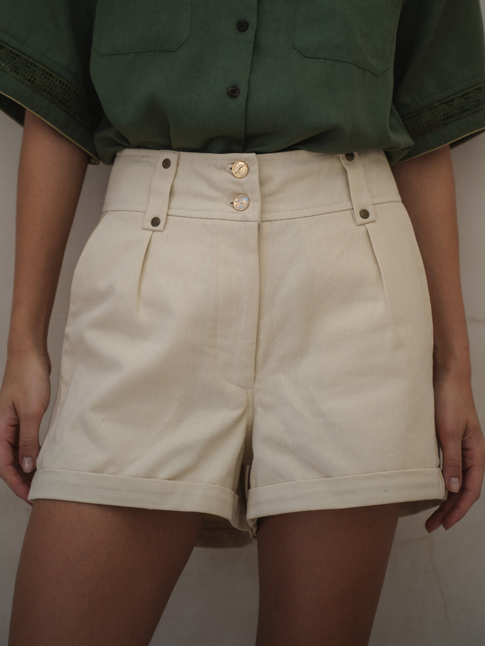 Beige shorts worn with a green shirt against a neutral background