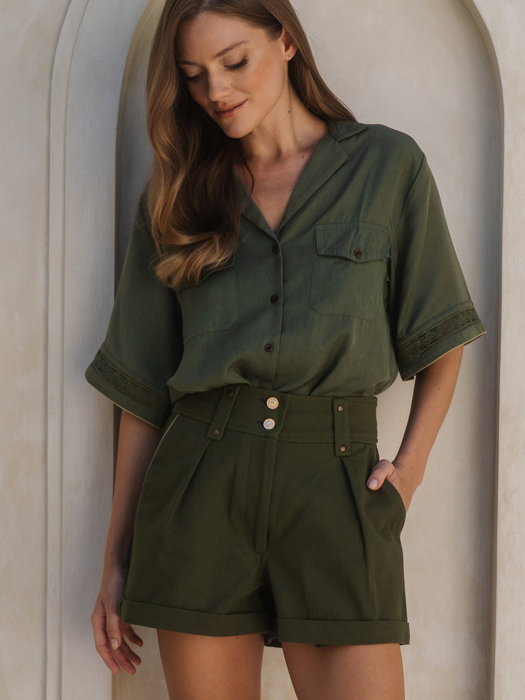 Woman wearing a green shirt and shorts set against a neutral background