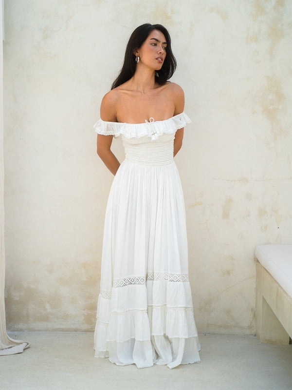 Woman wearing a white off-shoulder dress against a plain background