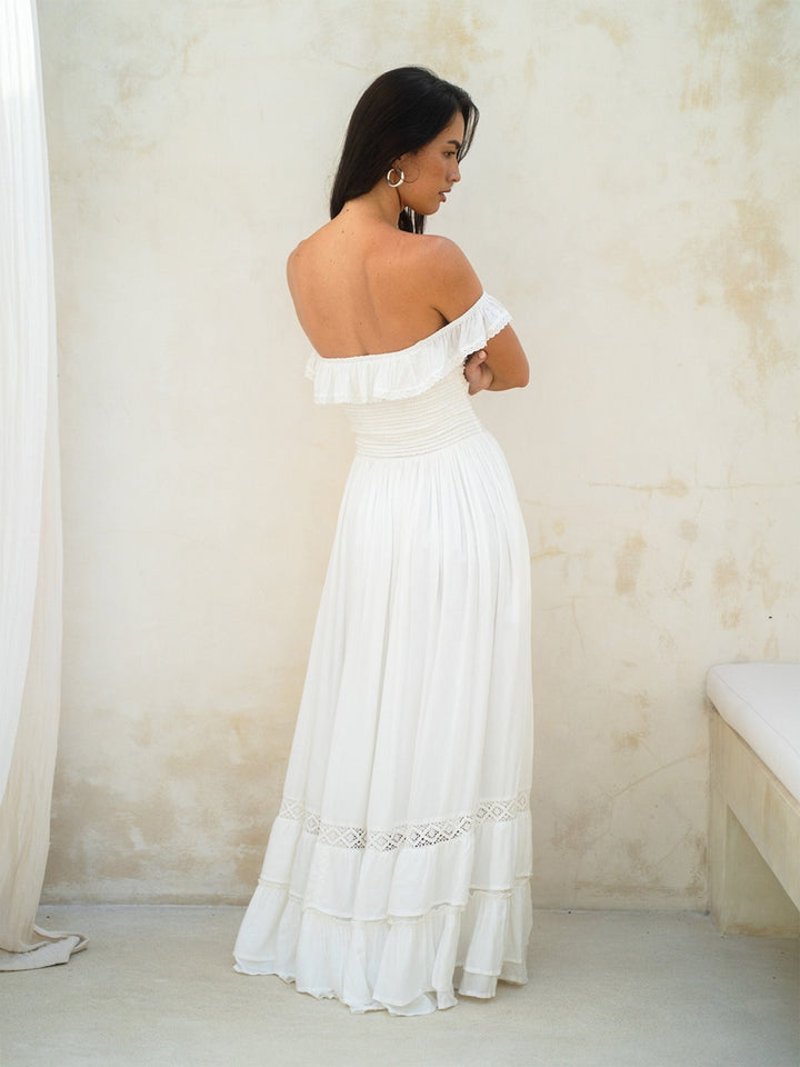 Woman wearing a white off-shoulder dress against a plain wall.