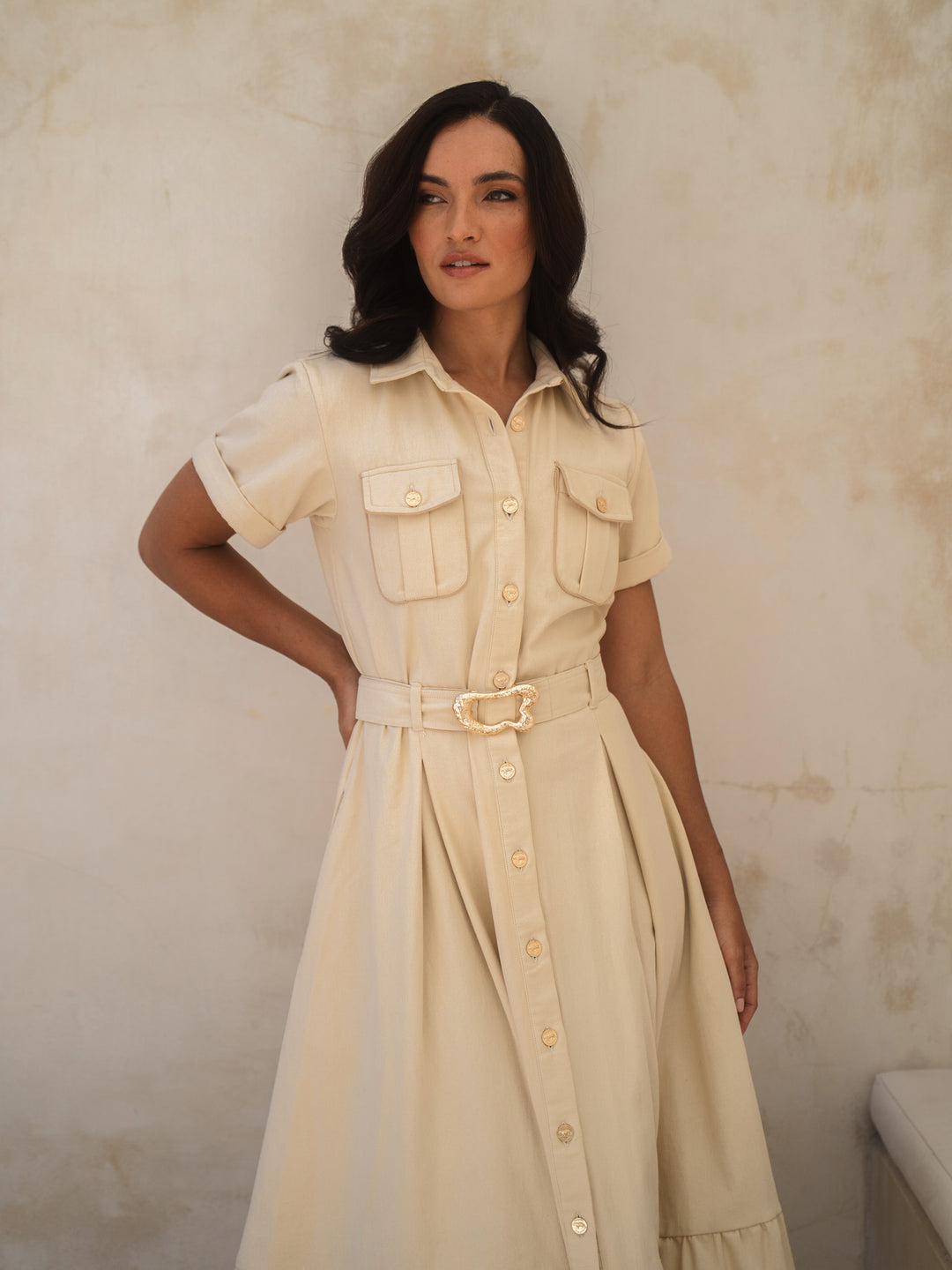 Woman wearing a beige dress with a belt against a plain background