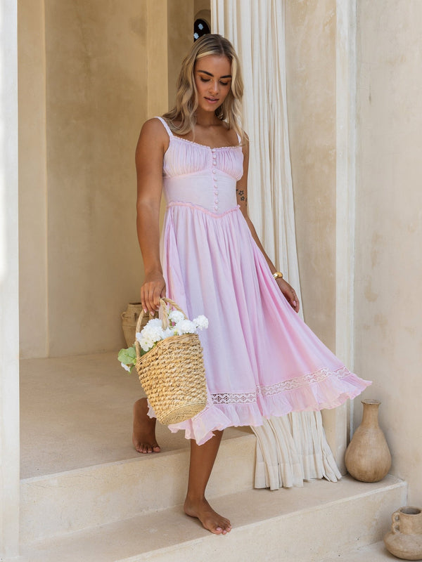 Woman in a pink dress holding a woven basket with flowers, standing on steps.