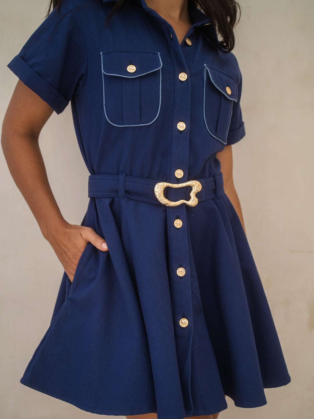 Navy blue dress with gold buttons and belt on a neutral background