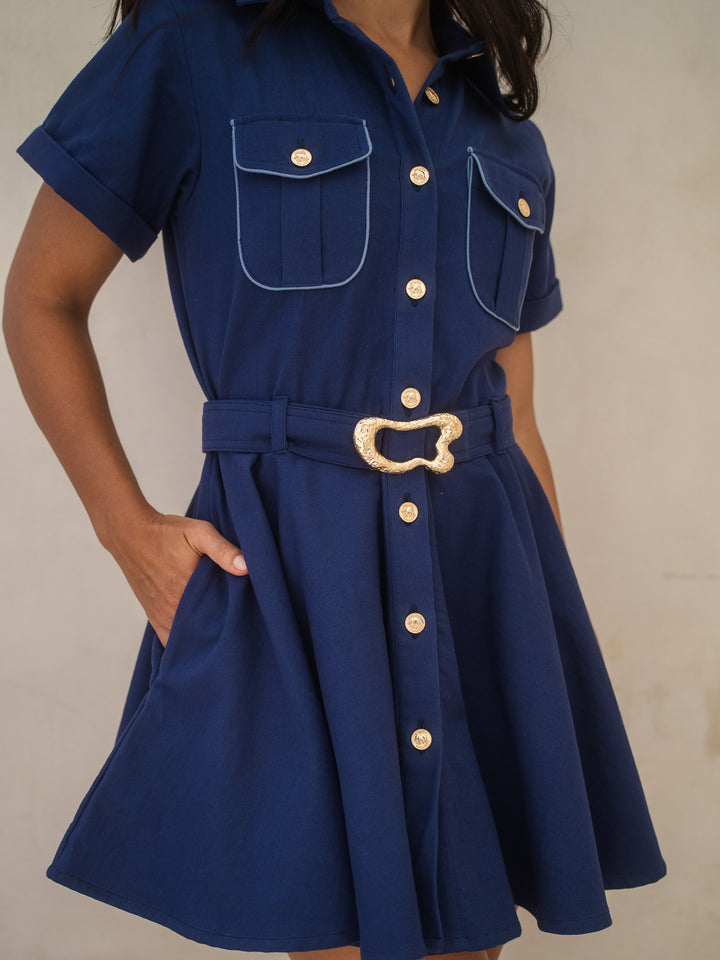 Navy blue dress with gold buttons and belt on a neutral background