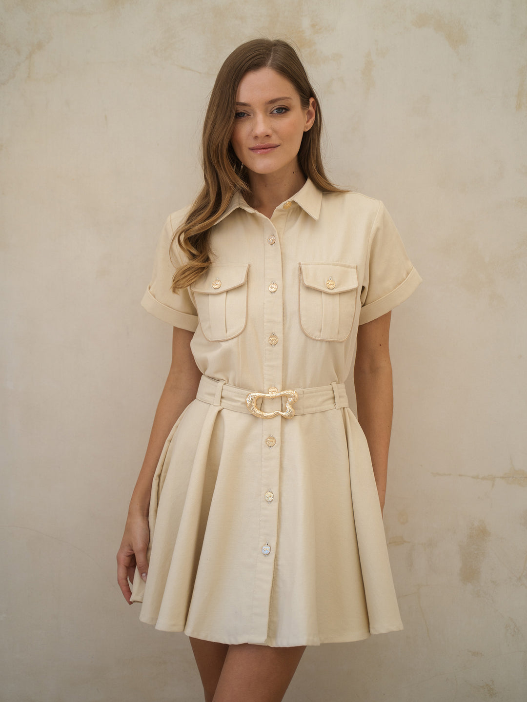 Woman wearing a beige dress with a belt against a plain background