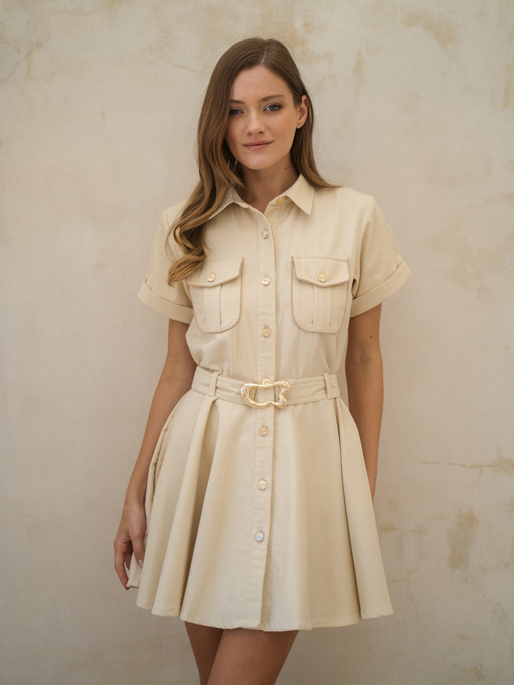 Woman wearing a beige dress with a belt against a plain background