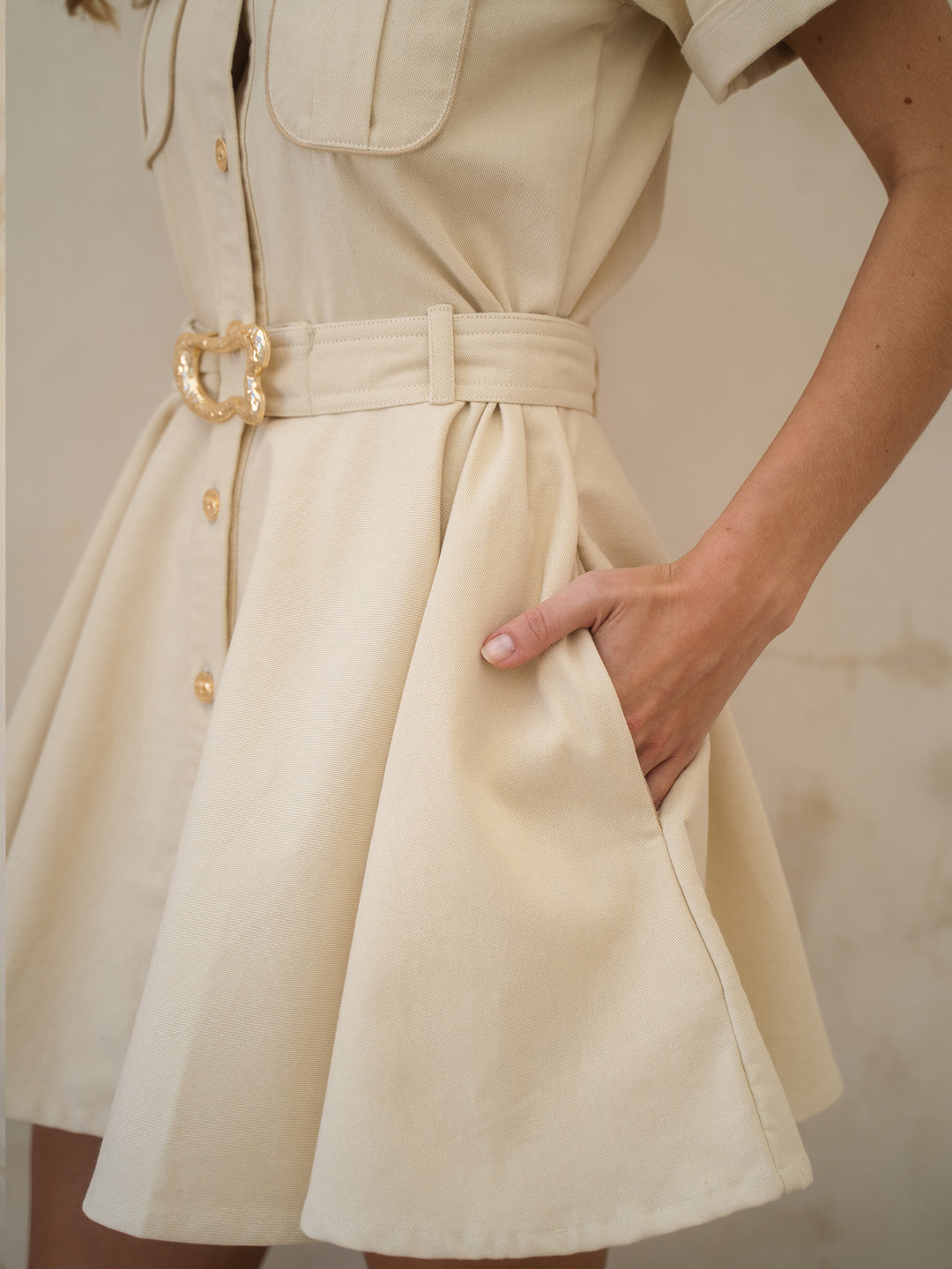 Beige dress with a gold belt and buttons on a neutral background