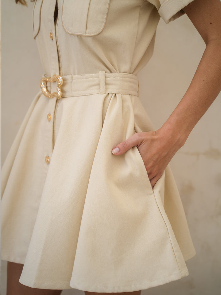 Beige dress with a gold belt and buttons on a neutral background