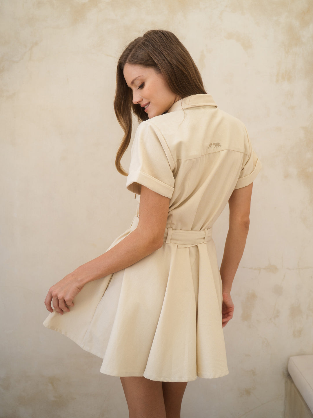 Woman wearing a beige dress against a textured wall.