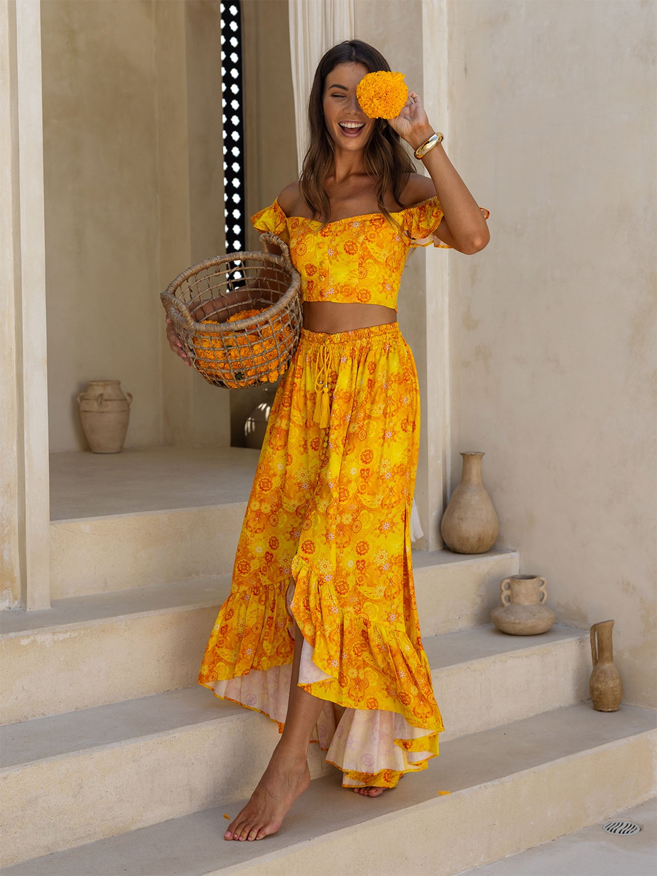Woman in a yellow floral dress standing on steps with decorative vases in the background