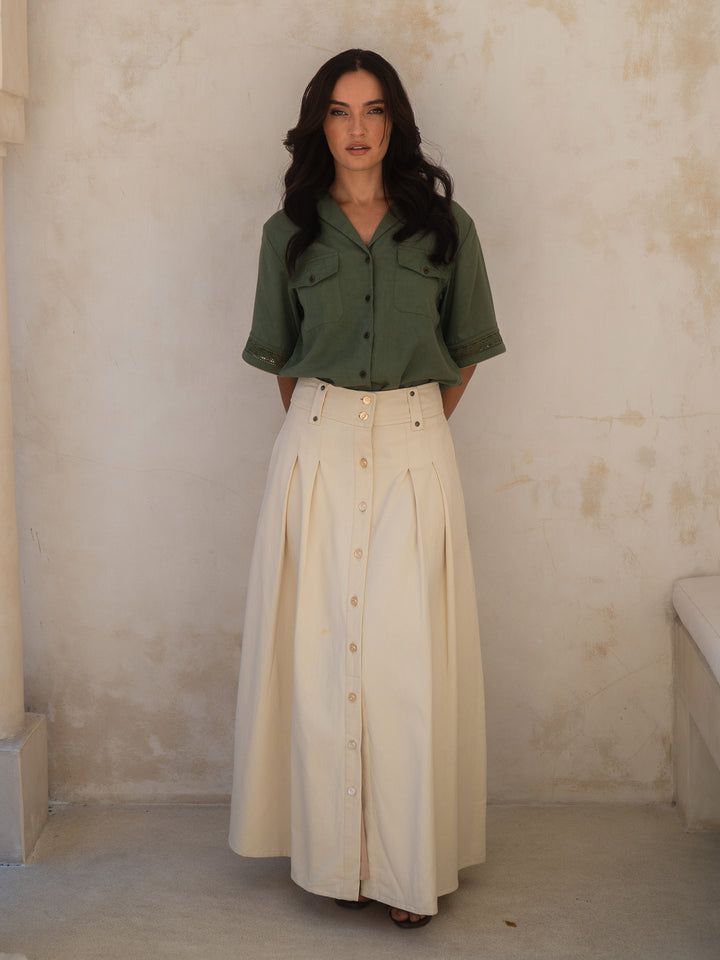 Woman wearing a green shirt and beige skirt against a textured wall.