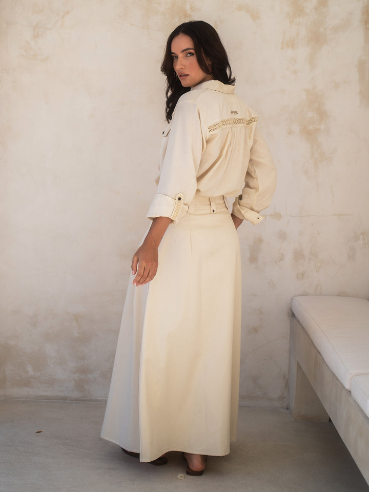 Woman wearing a long cream coat standing against a textured wall.