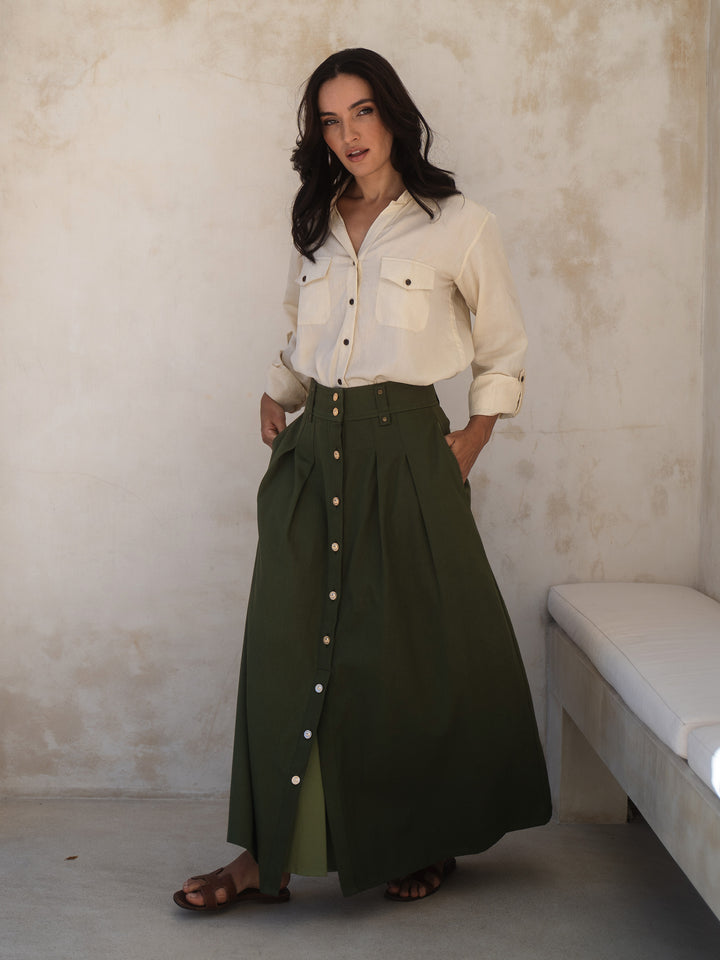 Woman wearing a white blouse and green skirt against a plain wall.