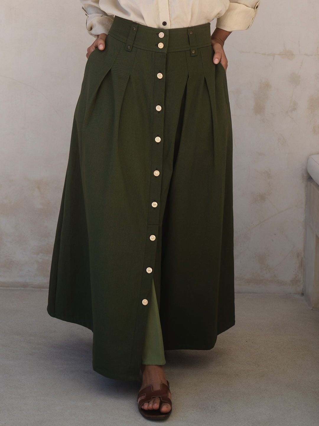 Person wearing a long green skirt with button details against a plain background