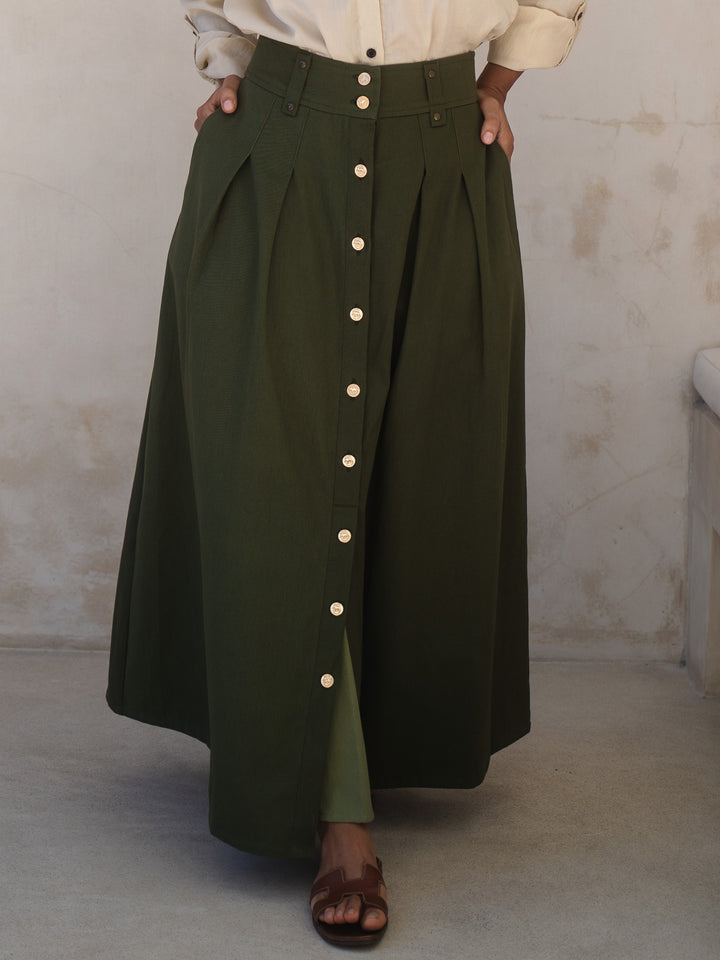 Person wearing a long green skirt with button details against a plain background