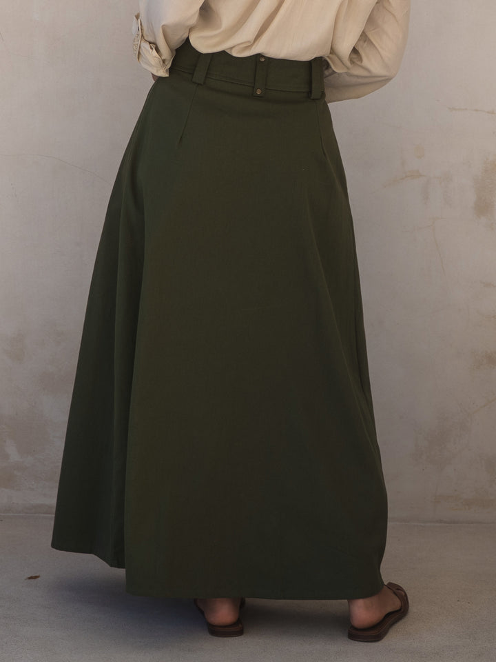Person wearing a long green skirt against a plain background