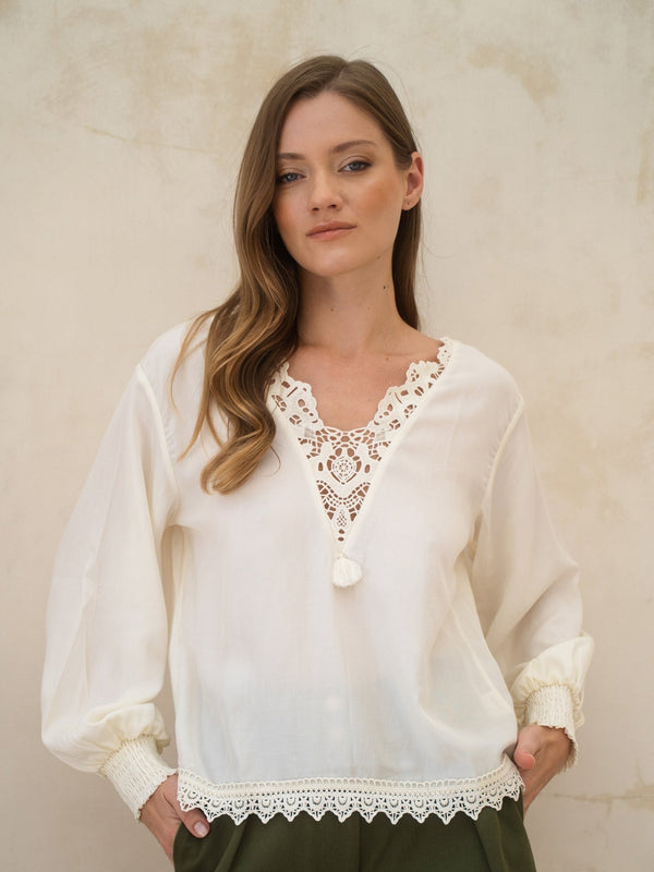 Woman wearing a white blouse with lace details against a beige background