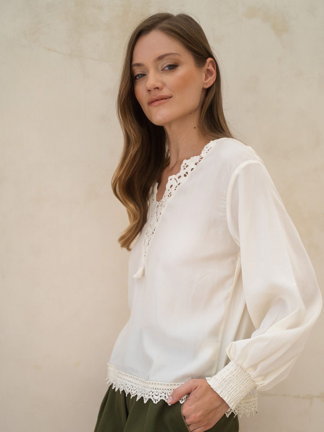 Woman wearing a white blouse with lace details against a beige background