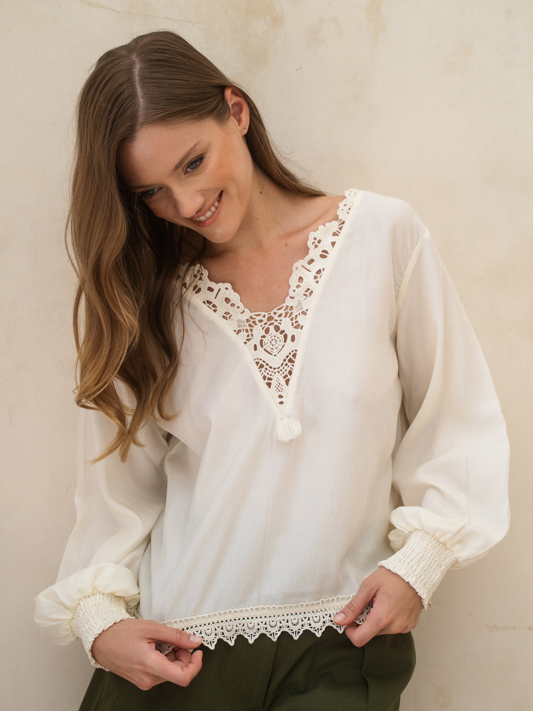 Woman wearing a white blouse with lace details against a beige wall