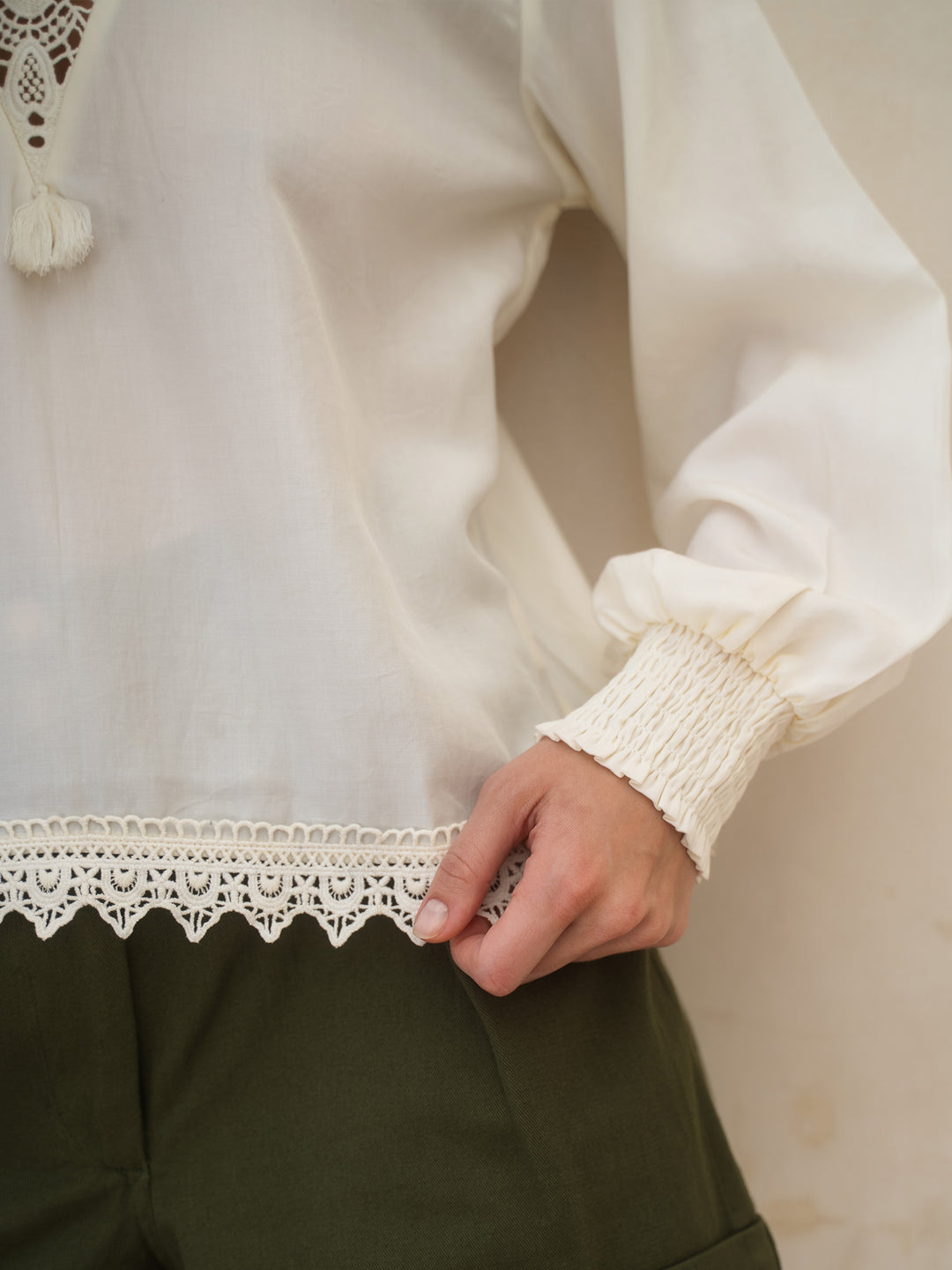 Close-up of a person wearing a white blouse with lace details and green pants.
