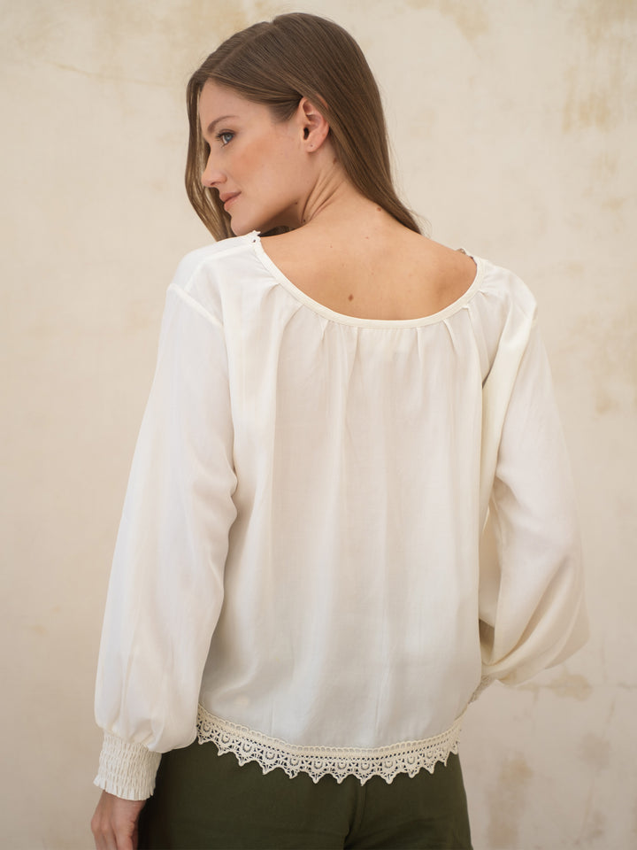 Woman wearing a white blouse with lace trim against a beige wall