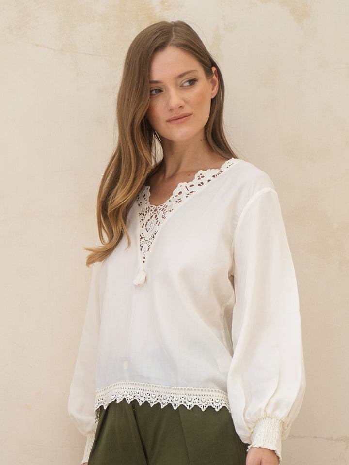 Woman wearing a white blouse with lace details against a beige background