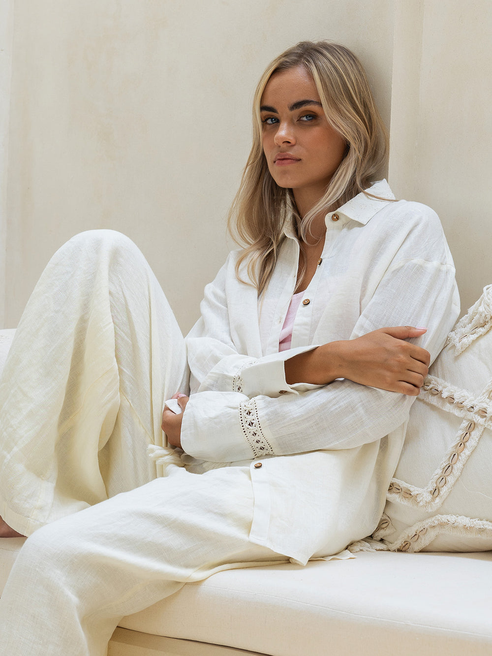 Woman in a white outfit sitting on a beige couch.
