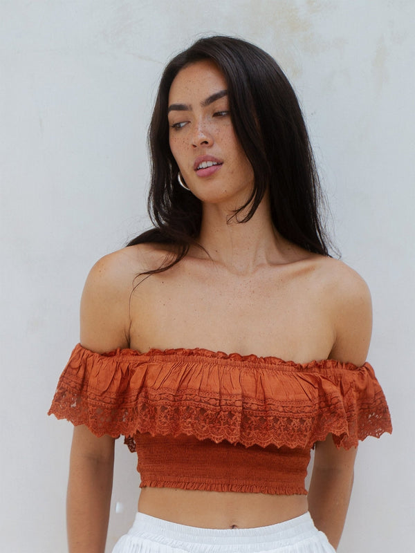Woman wearing an off-shoulder rust-colored top against a light background
