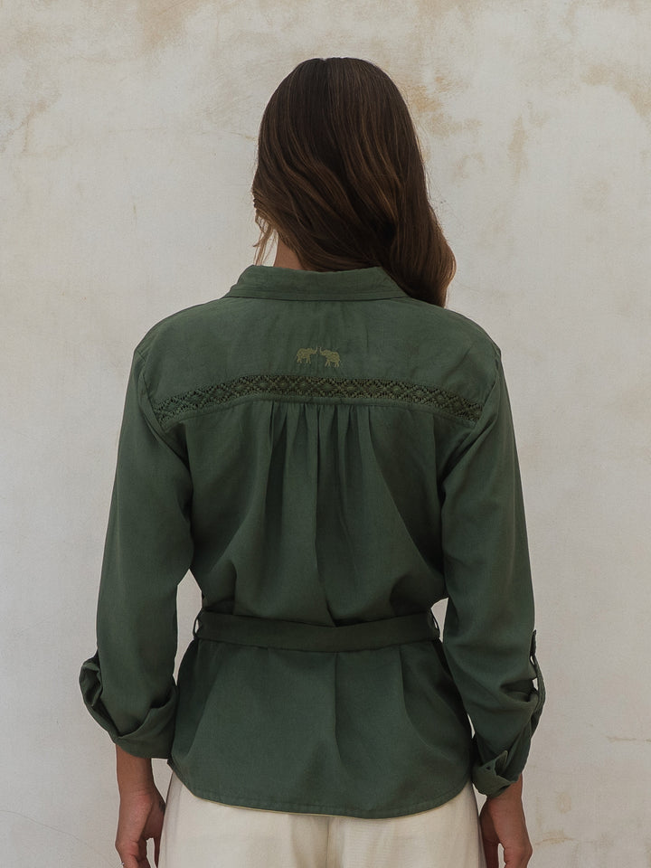 Person wearing a green jacket with braided details on a beige background