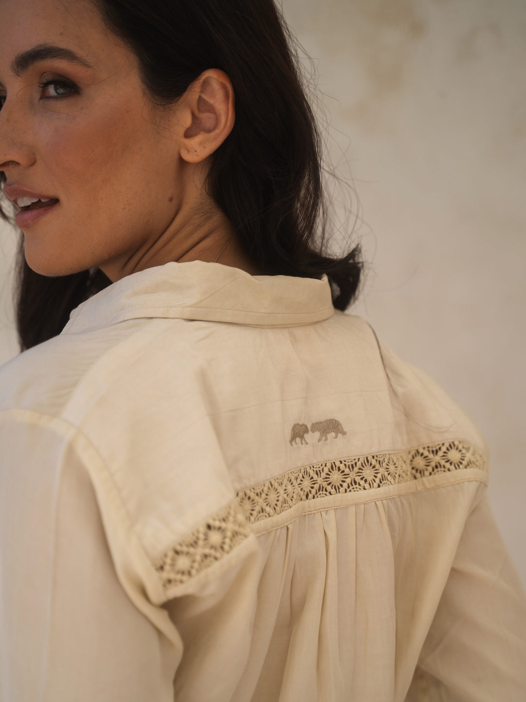 Woman wearing a beige embroidered blouse with a plain background