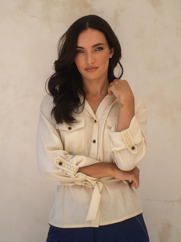 Woman wearing a cream-colored shirt with lace details against a beige background