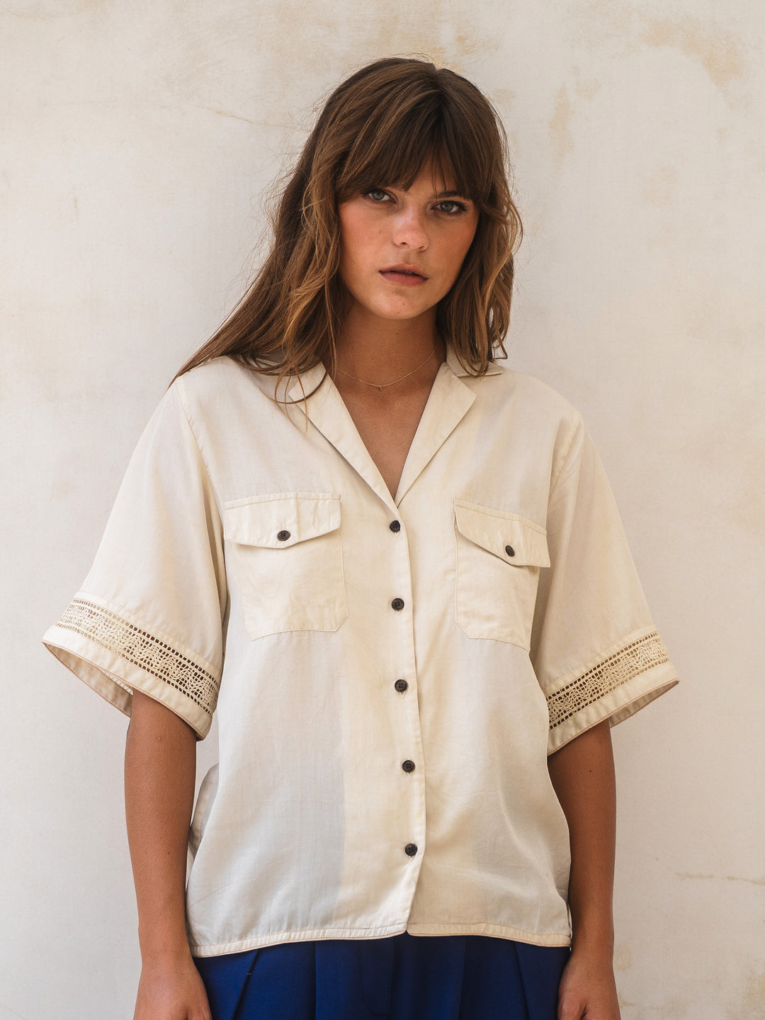 Woman wearing a cream-colored shirt with black buttons against a light background
