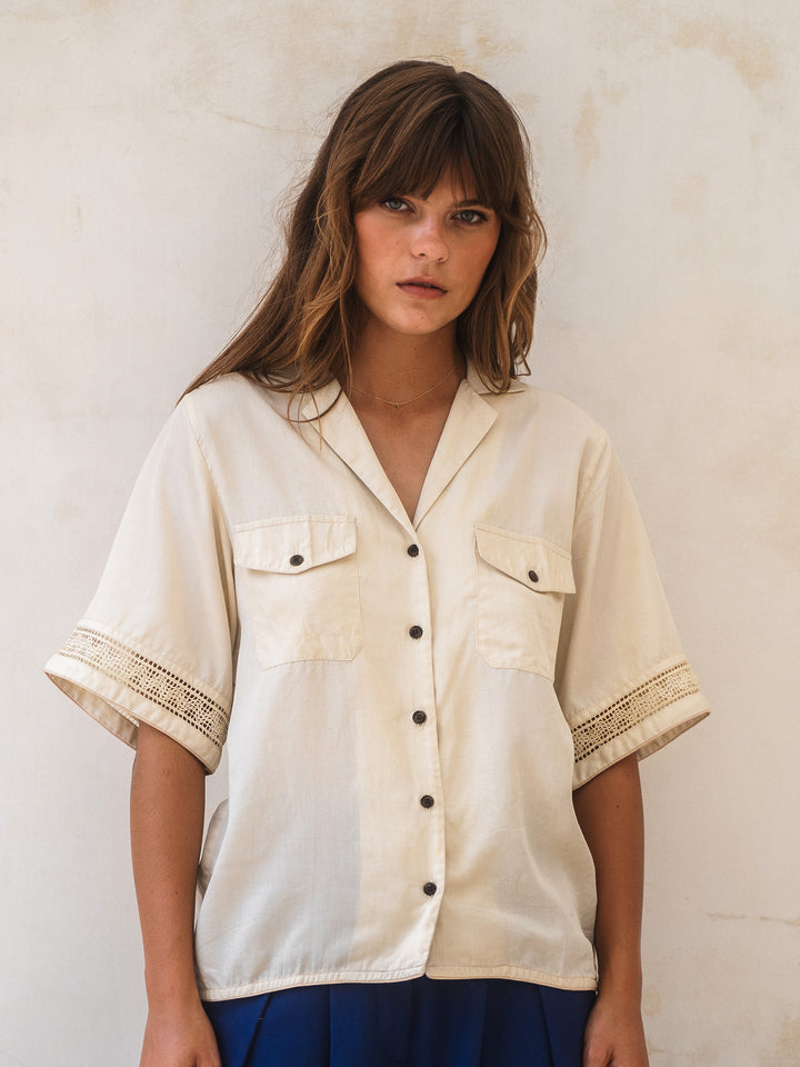 Woman wearing a cream-colored shirt with black buttons against a light background
