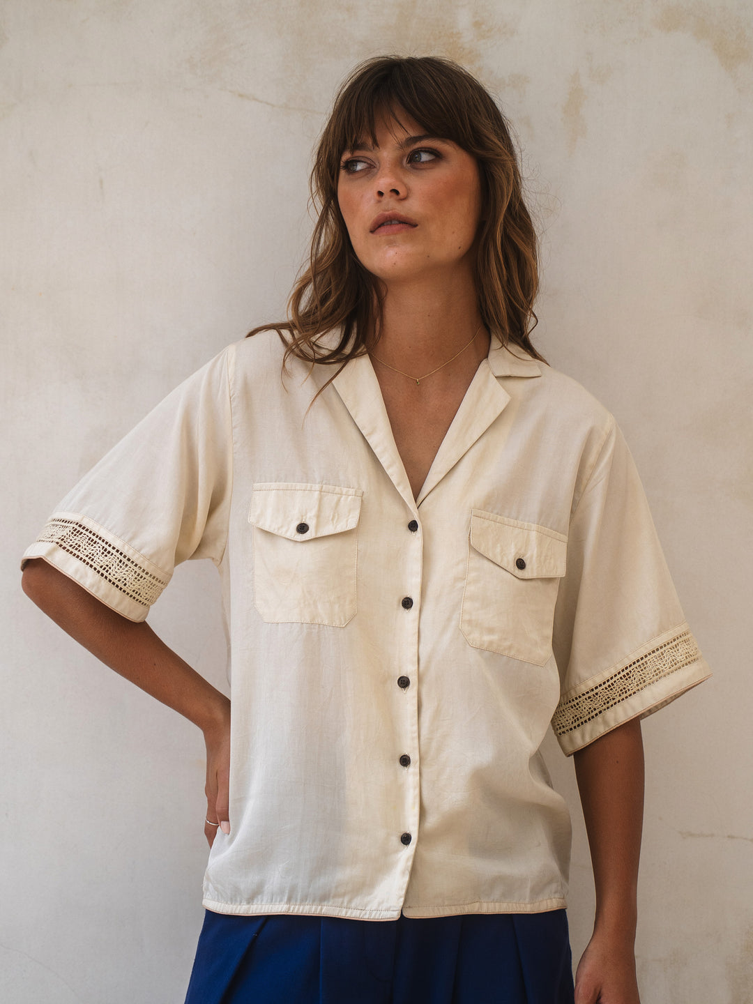 Woman wearing a beige shirt with lace trim against a plain background