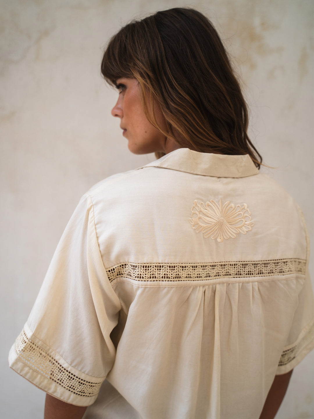 Woman wearing a cream-colored blouse with lace details against a plain background