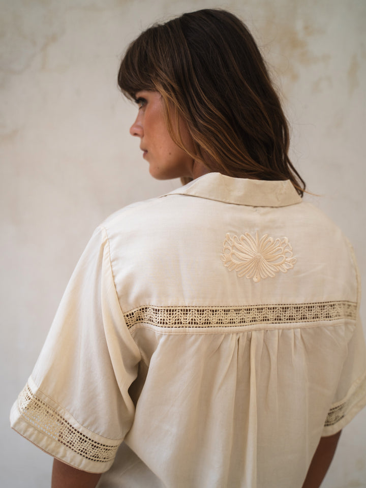 Woman wearing a cream-colored blouse with lace details against a plain background