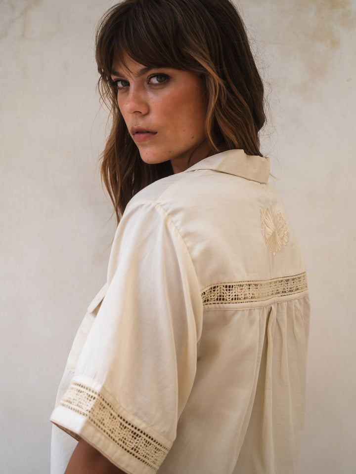 Woman wearing a beige embroidered blouse against a neutral background