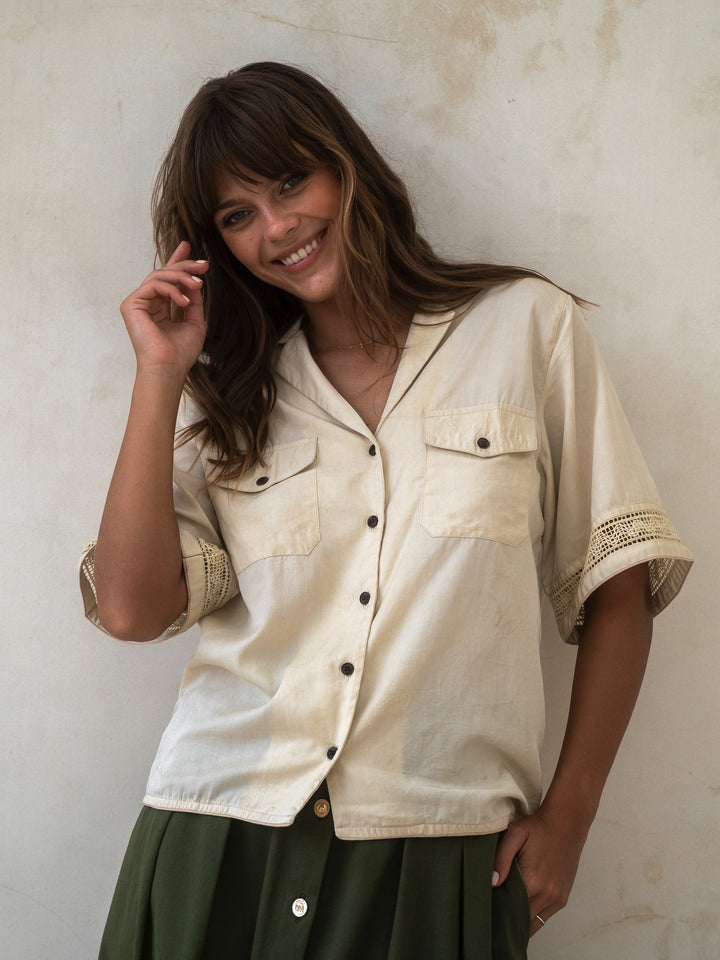 Woman wearing a beige shirt with black buttons against a textured wall.