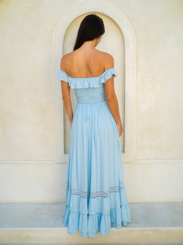 Woman wearing a light blue off-shoulder dress standing in front of an archway.