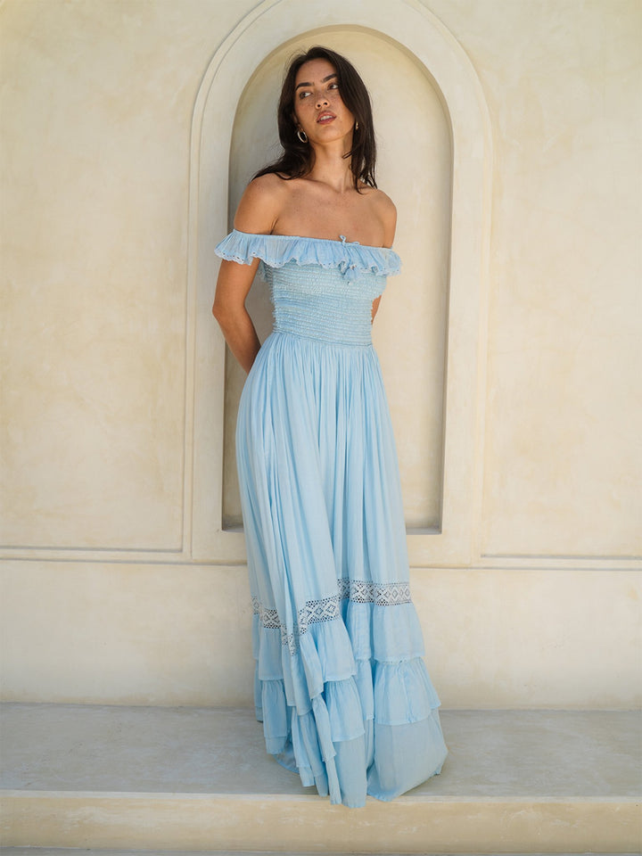 Woman wearing a light blue off-shoulder dress standing in front of an arched doorway.